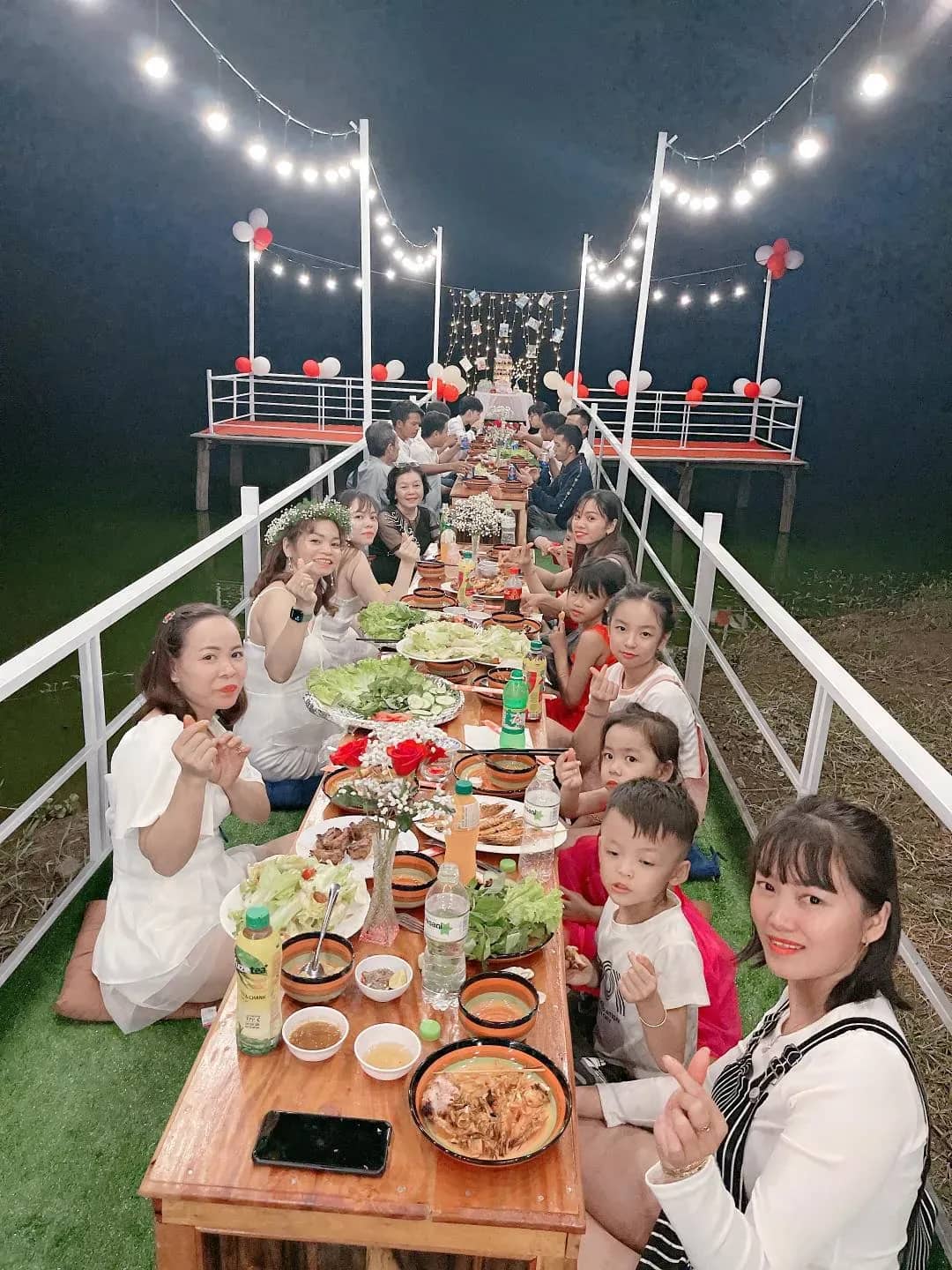 Bàn tiệc dài trên lối đi gỗ giăng đèn về đêm