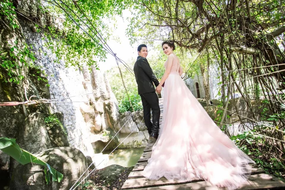 Cô dâu chú rể trên cầu gỗ bên tường đá và dòng nước chảy